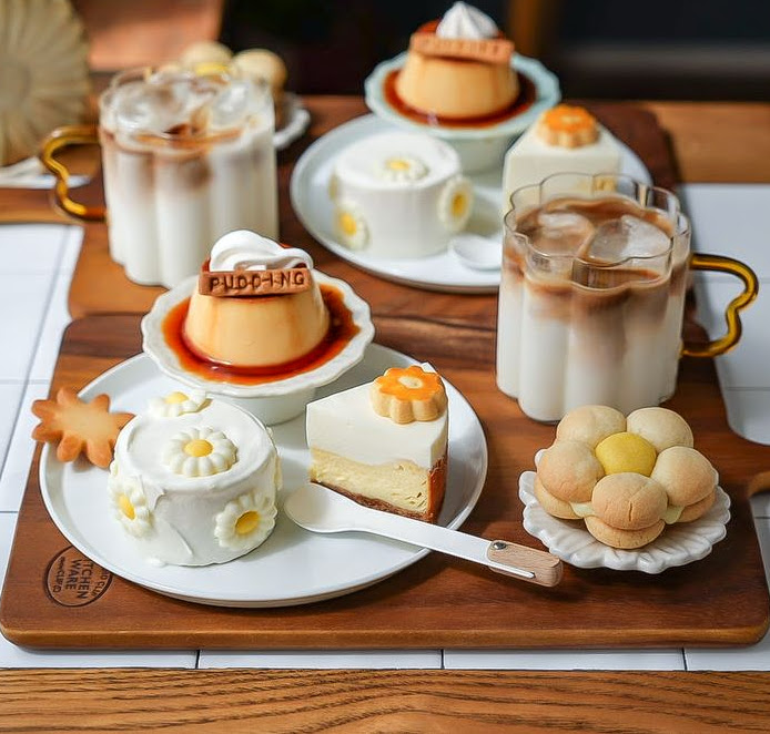Iced lattes and assorted desserts on a wooden tray, including flan pudding and cheesecake