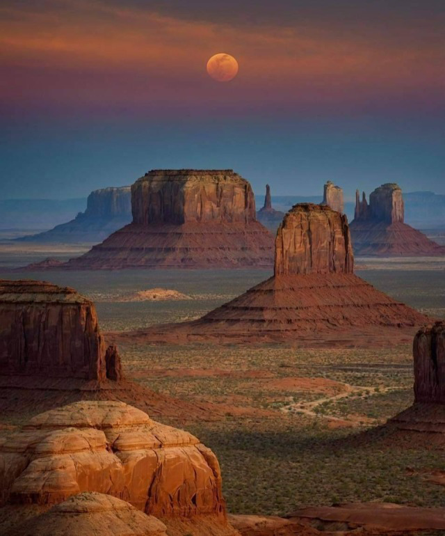 Full moon rising over Monument Valley sandstone buttes at dusk with red desert landscape