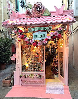 Pink ornate antique shop storefront with decorative awning and floral accents in narrow alley