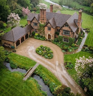 Aerial view of an old English manor house with gardens, driveway, and small stream