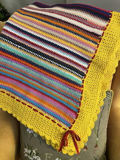 Colorful striped crochet blanket with yellow scalloped edge draped over a grey chair