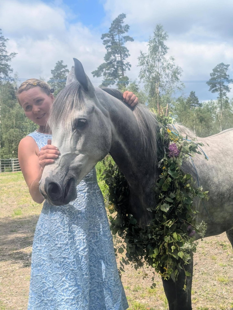 Young girl posing beside a gray horse with a leafy floral garland outdoors
