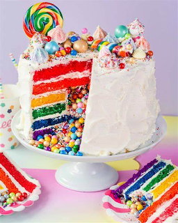 Rainbow layer cake with candy filling, lollipops, and sprinkles on a white stand