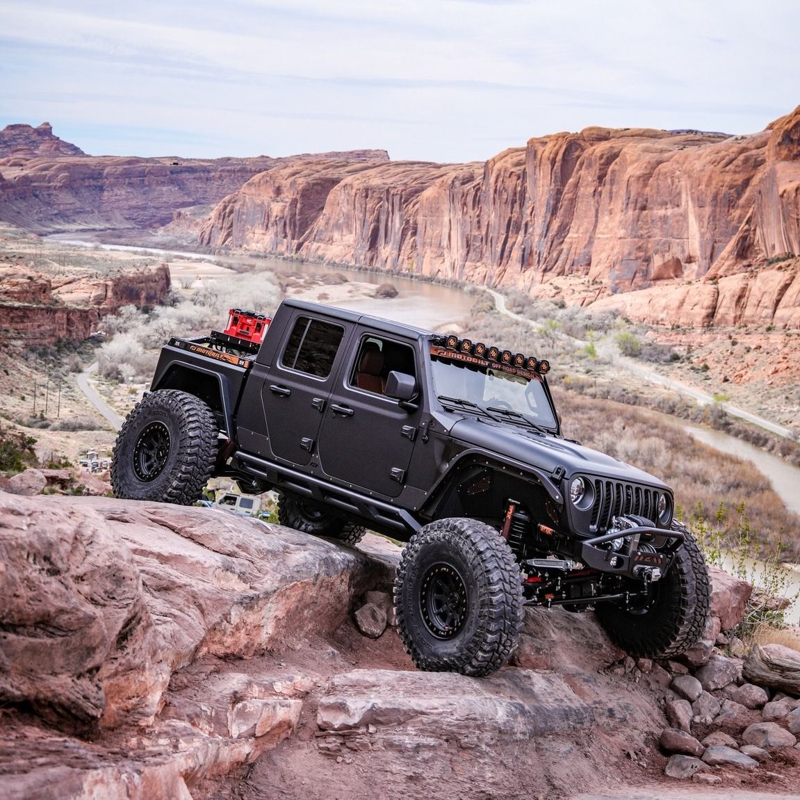 Black off-road jeep on rocky desert trail with red canyon cliffs in the background