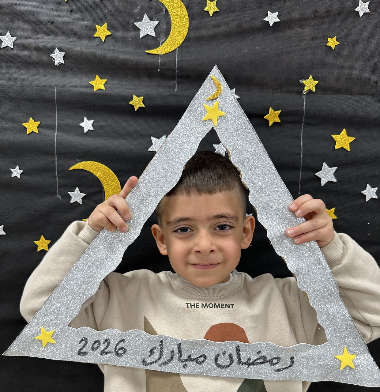 Smiling boy holding a triangular Ramadan-themed frame with stars and crescent moons