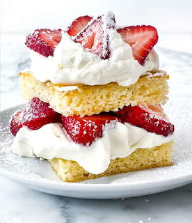 Layered strawberry shortcake with whipped cream, sliced strawberries, and powdered sugar on a plate