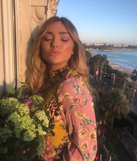 Young woman in floral top on a balcony overlooking a coastal beach scene at sunset