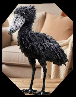 Black crocheted shoebill stork with fuzy textured yarn and gray beak standing on wooden surface