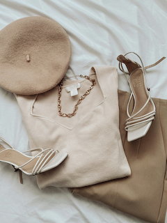 Beige fashion flat lay with heels, beret, handbag, necklace, and trousers on white fabric