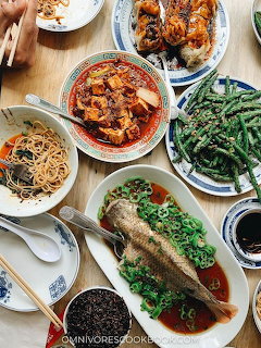 Overhead shot of a Chinese meal with steamed fish, green beans, noodles, and spicy dishes on a table