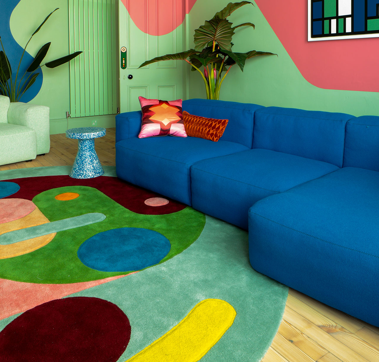 Colorful living room with a blue sectional sofa, abstract rug, mint walls, and plants
