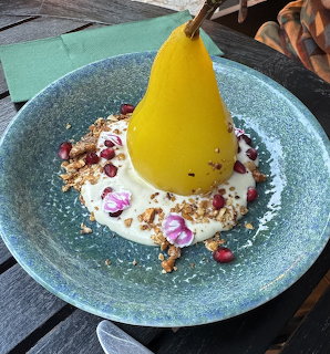 Yellow poached pear dessert with cream, granola and flowers on blue speckled plate