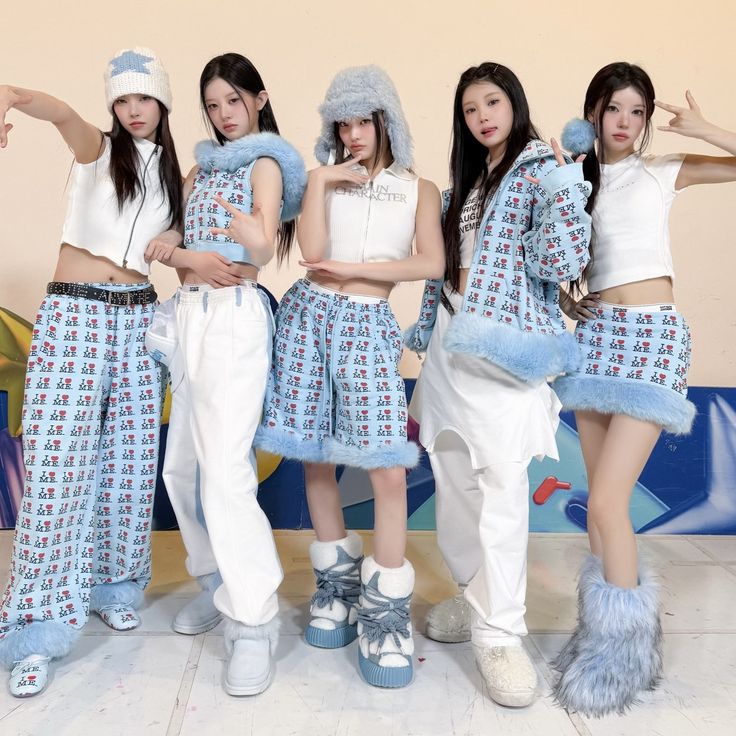 Five women in matching white and blue streetwear outfits posing together indoors