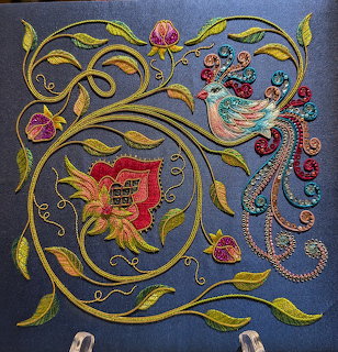 Colorful embroidered bird and flower with swirling vines on blue fabric