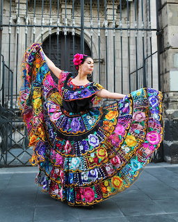 Woman dancing in colorful traditional Mexican dress with floral embroidery in front of historic building