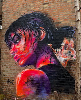 Street art mural of a woman with dark hair and a fox painted in vibrant pink and purple on a brick wall