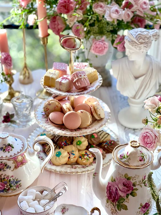 Tiered dessert stand with macarons and pastries on elegant table with pink roses and vintage teaware