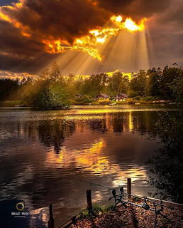 Golden sunset with rays of light breaking through clouds reflected on a tranquil lake surrounded by trees