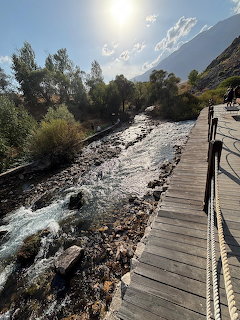 Wooden footbridge over a rushing rocky mountain river with sunlit peaks and green trees in background