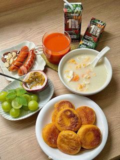 Korean breakfast with pancakes, congee, sausages, grapes, passion fruit, orange juice and milk cartons on a table