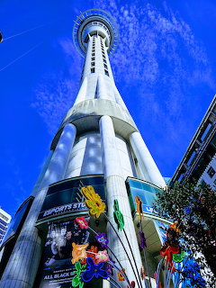 Auckland Sky Tower viewed from below against a bright blue sky with colorful street art at its base