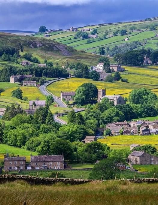 Rolling green hills dotted with stone houses and fields in countryside landscape