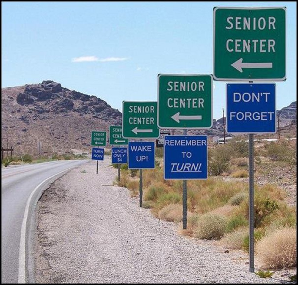 Row of repeating green Senior Center highway signs along desert road with mountain backdrop