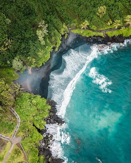Aerial view of turquoise waves washing into a rocky cove beside dense green tropical forest