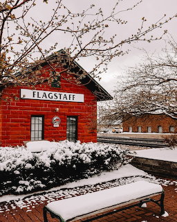 Snow-covered red brick Flagstaff train station with benches and bare trees in winter