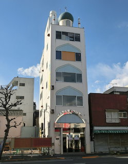 Tall white mosque building with green dome and minaret tower on a Japanese city street