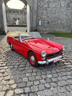 Red vintage MG Midget convertible parked on cobblestones before stone fortress wall