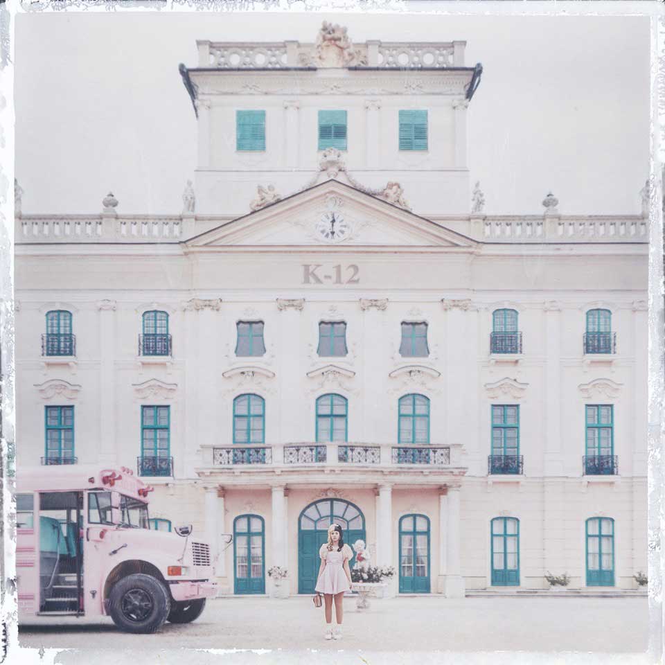 Girl in white dress standing before pastel pink neoclassical school building with turquoise windows and pink bus