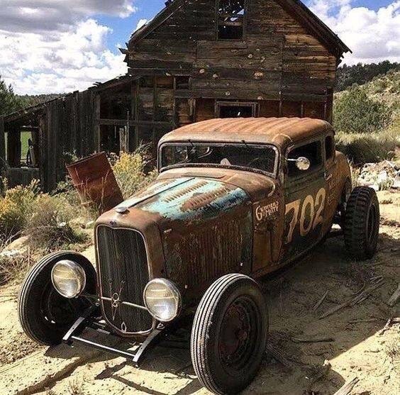 Rusty vintage hot rod car in front of old wooden barn