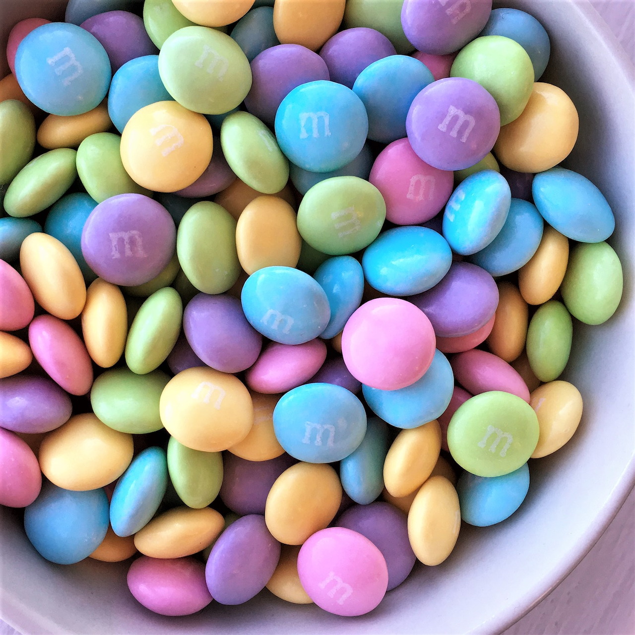 Bowl filled with pastel colored candy coated chocolate pieces in rainbow colors