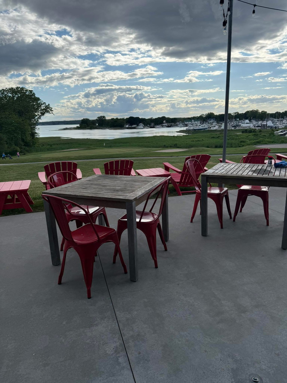 Outdoor patio with red chairs and wooden tables overlooking a lake and green lawn at dusk.