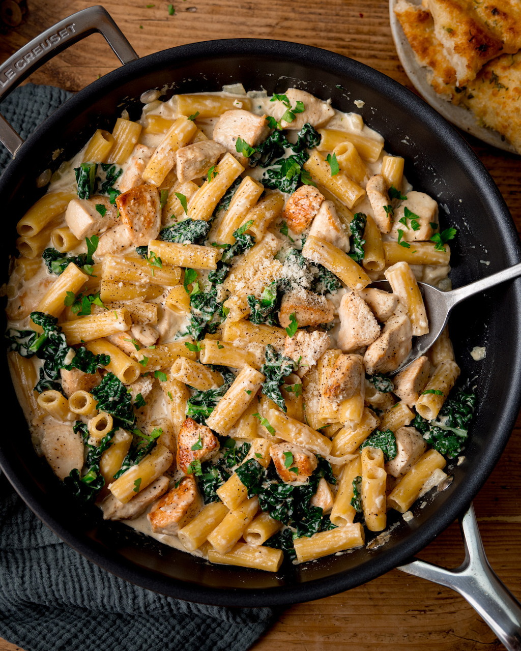 Cast iron skillet with creamy chicken and kale rigatoni pasta topped with Parmesan cheese