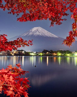Mount Fuji with snow-capped peak framed by red autumn foliage over calm lake at dusk