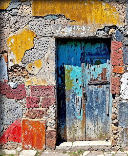 Weathered blue wooden door in deteriorating colorful wall with peeling paint and exposed brick