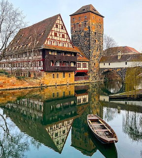 Half-timbered buildings and tower reflected in river with wooden boat in Nuremberg Germany