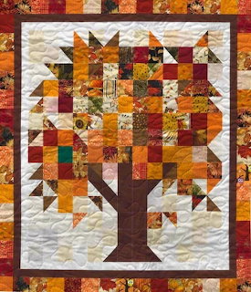 Handmade patchwork quilt depicting an autumn tree with geometric fabric squares in warm fall colors