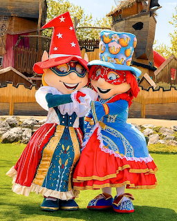Two theme park mascot characters in colorful costumes with large hats posing together outdoors