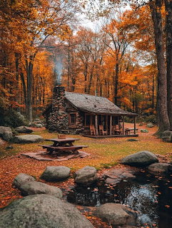 Rustic log cabin with stone chimney surrounded by orange and gold autumn trees with a pond in front