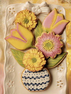 Decorated sugar cookies shaped like yellow tulips, pink flowers, and a blue vase on a white plate