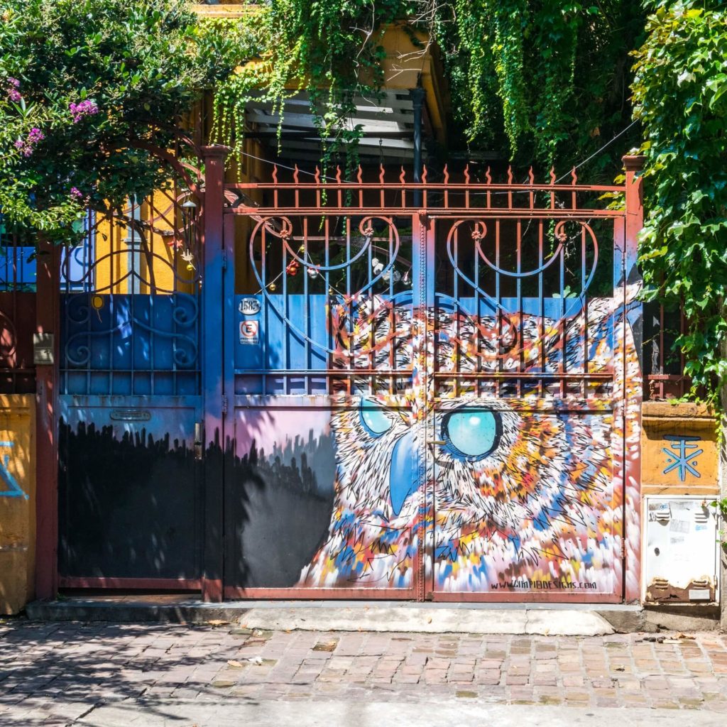 Ornate gate with blue doors and colorful mosaic tiles surrounded by ivy and purple flowers in Buenos Aires