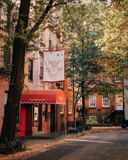 Tree-lined city street with brick buildings, red storefront awning, and autumn foliage