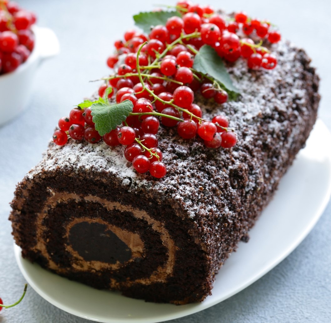 Chocolate roll cake with powdered sugar, red currants, and leaves on white plate