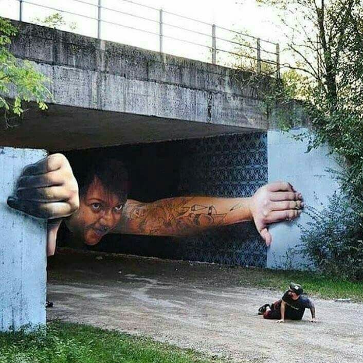 Surreal underpass mural of a giant man reaching out beneath a bridge near a small seated person