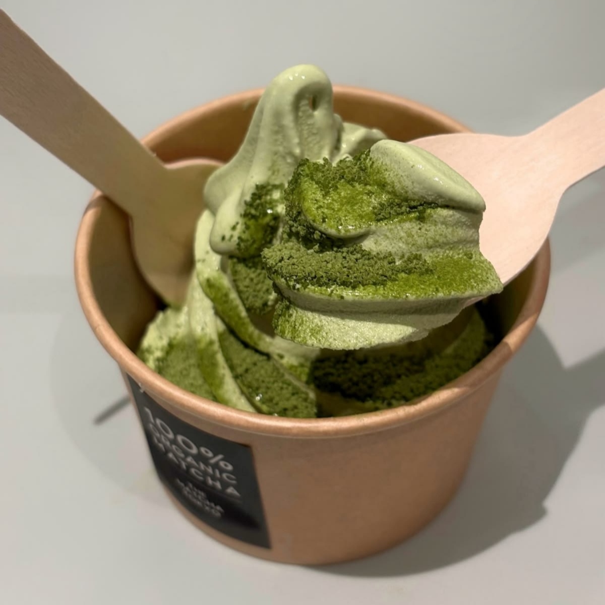 Cup of matcha ice cream with matcha powder and two wooden spoons
