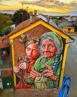Street art mural of a girl and an elderly woman painted on the side of a building in an Italian town