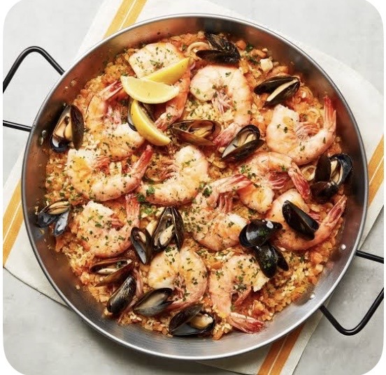Pan of seafood paella with shrimp, mussels, rice, and lemon wedges